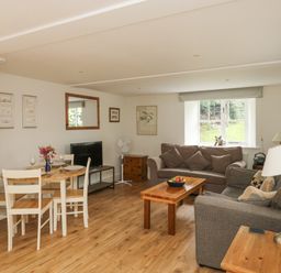 A living room with dining table, chairs, sofas, coffee table, TV, and window at Ixworth Cottage in Little Woodford near Ottery St Mary