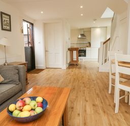 A living area with a bowl of fruit on a wooden coffee table and a kitchen in the background at Ixworth Cottage in Little Woodford near Ottery St Mary
