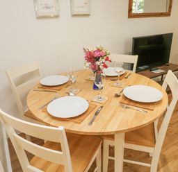 A dining area with a round wooden table set for four with plates glasses and cutlery at Ixworth Cottage in Little Woodford near Ottery St Mary