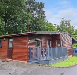 A wooden cabin with a small porch and outdoor seating surrounded by trees and grass at Ramson in Saltburn-By-The-Sea
