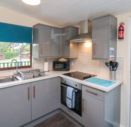 A kitchen with grey cabinets a window with a blue blind a sink stove oven microwave and kitchen utensils at Ramson in Saltburn-By-The-Sea