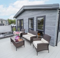 An outdoor patio with wicker furniture a glass table a hot tub and flowers at Sunset Lodge in Woodhall Spa