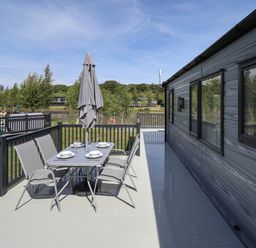 An outdoor deck with a dining table set with plates and glasses next to a building at Sunset Lodge in Woodhall Spa