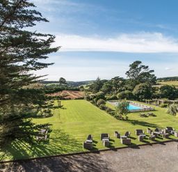 An outdoor area with lawn chairs tables a swimming pool and trees at Alston Hall in Battisborough Cross