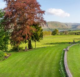 A garden with trees lawn sculpture and swing set overlooking hills and water at Bank Barn Wreay in Watermillock