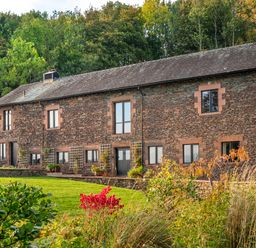 A stone house with multiple windows and greenery in front at Bank Barn Wreay in Watermillock