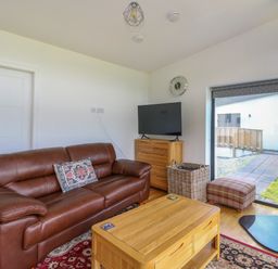 A living room with a brown leather sofa a wooden coffee table a television on a wooden dresser a plaid footstool and a wood stove at 6 Strathtay Lodges Aberfeldy