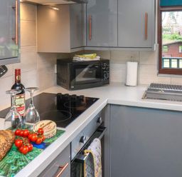 A kitchen with gray cabinets a black microwave a stovetop a bread loaf tomatoes a bottle of wine and two wine glasses at Cowslip in Saltburn-By-The-Sea
