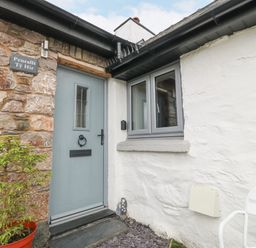An entrance door with a window next to it and a stone wall with a sign on a white house at Penrallt in Rhydlydan