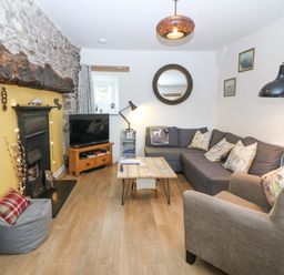 A living room with a stone fireplace a gray couch a wooden coffee table and a TV at Penrallt in Rhydlydan