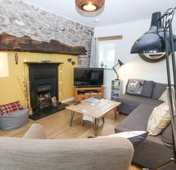 A living room with a stone wall fireplace television wooden coffee table and grey sofa at Penrallt in Rhydlydan