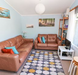 A living room with two brown leather sofas a patterned rug a small white TV stand with a television and a wooden shelving unit at Milkwood in Elmrise Park near Llansteffan