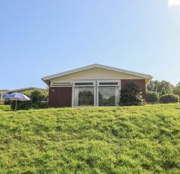 A small house with large windows on a grassy slope at Milkwood in Elmrise Park near Llansteffan