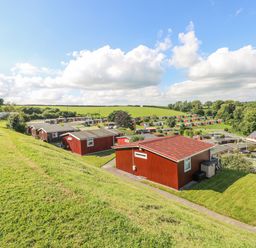 A hillside view of red wooden cabins with green lawns and trees at Milkwood in Elmrise Park near Llansteffan