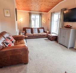 A living room with brown leather sofas a wall mounted television and a cabinet at Brightwater Lodge White Cross Bay near Windermere