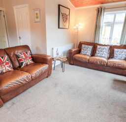 A living room with two brown leather sofas a small wooden side table and a window with checkered curtains at Brightwater Lodge White Cross Bay near Windermere