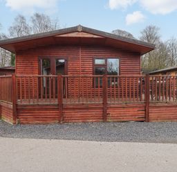 A wooden cabin with a fenced deck and gravel driveway at Brightwater Lodge in White Cross Bay near Windermere