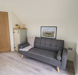A gray sofa with a blanket and cushions next to a wooden door and a small cabinet with flowers and a heart decoration at Shepherds View in Castlerigg near Keswick