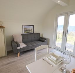 A living room with a gray sofa and a small green cabinet near glass double doors at Shepherds View in Castlerigg near Keswick