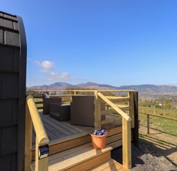 An outdoor wooden deck with wicker chairs and a table overlooking hills and fields at Shepherds View Castlerigg near Keswick