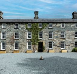 A stone building with multiple windows and a gravel driveway at Snowdonia Manor in Dolgellau