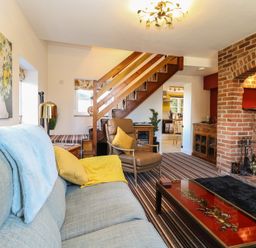 A living room with a sofa chair staircase and brick fireplace at Cobble Cottage in Great Ryburgh