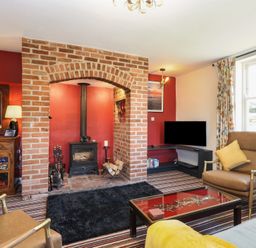 A living room with a brick fireplace wood stove leather chairs striped carpet and a television at Cobble Cottage in Great Ryburgh