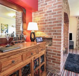 A wooden sideboard with a mirror lamp and cocktail shaker set next to a brick fireplace in a living room at Cobble Cottage in Great Ryburgh