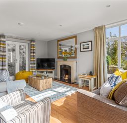 A living room with sofas a striped armchair a coffee table fireplace and large windows at Seascape in Kingsand