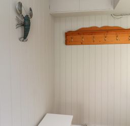A white paneled room with a wooden coat rack and a lobster wall decoration at Aln Cottage Alnmouth