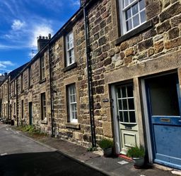 A stone row house with multiple front doors and windows on a narrow street at Aln Cottage in Alnmouth