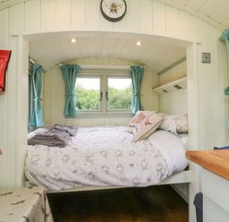 A small bedroom with a double bed surrounded by windows with blue curtains and a wooden countertop at Cuckoo's Nest in South Molton