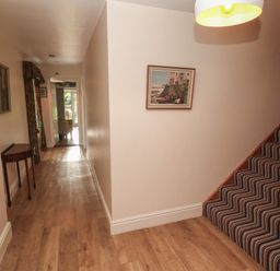 A hallway with wooden floor a striped carpeted staircase a small table and framed paintings at Tremornah in Lamorna