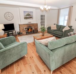 A living room with green sofas a stone fireplace a wooden coffee table and a television at Tremornah in Lamorna