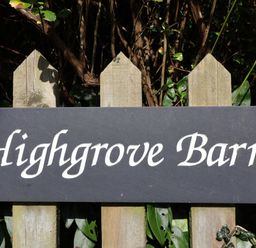 A wooden fence with a sign reading Highgrove Barn surrounded by leaves and branches at Highgrove Barn in Painswick