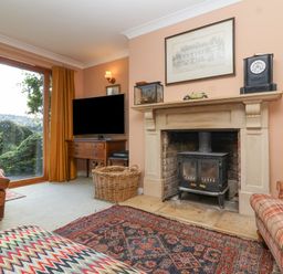 A living room with a fireplace a television and sliding glass doors showing greenery at Highgrove Barn in Painswick