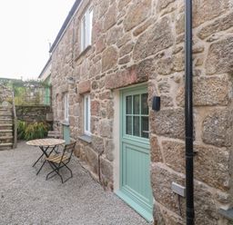 An outdoor area with a table and chair near stone walls at Mys Hedra Farm in St Buryan