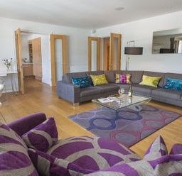 A living room with a gray sectional sofa with colorful pillows a purple patterned armchair and a glass coffee table at 21 Dart Marina in Dartmouth
