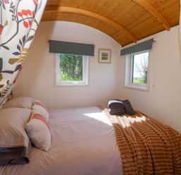 A bedroom with a bed and windows at Higher Merther Farm Shepherds Hut in Helston