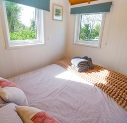 A bedroom with a double bed and windows at Higher Merther Farm Shepherds Hut Helston