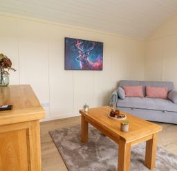 A living room with a gray sofa pink cushions a wooden coffee table a wooden cabinet and a painting of a deer at The View in Bangor-On-Dee