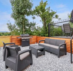 An outdoor seating area with black wicker furniture a grill and a patio with table and umbrella at The View in Bangor-On-Dee