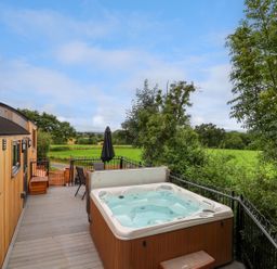 A wooden deck with a hot tub seating and table with umbrella overlooking green fields at The View in Bangor-On-Dee