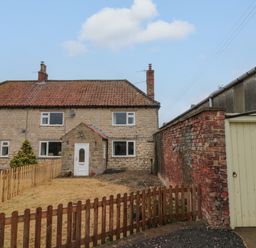 A stone house with a front yard and wooden fences next to a brick wall and gate at Bellmanear Farm Cottage in North Grimston near Malton
