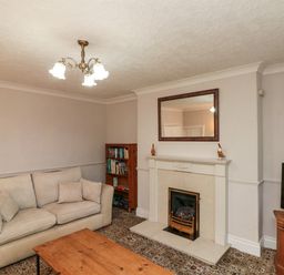 A living room with a beige sofa a wooden bookshelf a fireplace with a mirror above and a TV on a wooden stand at Bellmanear Farm Cottage in North Grimston near Malton