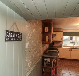 A kitchen with white cabinets, a window above the sink, tiled floor, and a wall sign saying farming is not a job at Bellmanear Farm Cottage in North Grimston near Malton