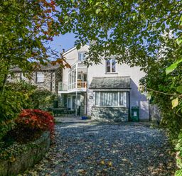 A white house with stone and glass features surrounded by trees and a gravel driveway at Blue Hill House in Ambleside