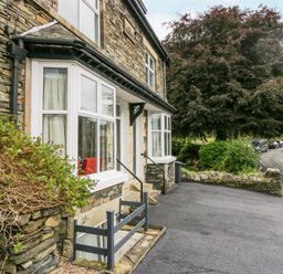 Stone house exterior with white windows and a paved driveway near a road with cars and trees at Park Beck 3 in Windermere