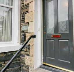 A front door with frosted glass panels and a mailbox on a stone wall next to a window at Park Beck 3 in Windermere