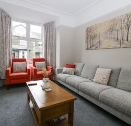 A sitting room with a grey sofa two orange armchairs a wooden coffee table and a triptych tree painting on the wall at Park Beck 3 in Windermere